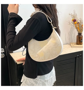 Detail view of a cream floral hobo bag worn by a model in an elegant indoor setting