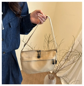 Detail of beige canvas crossbody bag featuring dual zippers and branded side label