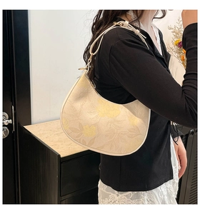 Detail of beige hobo bag with yellow floral print and gold metal strap buckles