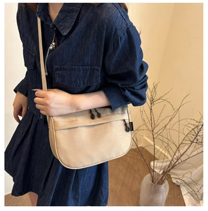 Detail of a beige canvas crossbody bag with zipper and black brand label