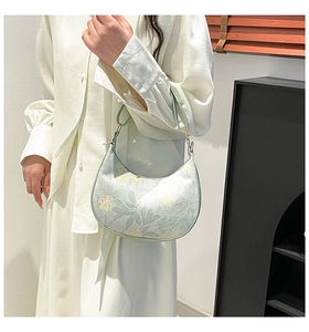 Close-up of a light green crescent bag with yellow floral patterns and sleek leather strap