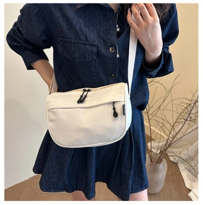 Close-up of cream canvas crossbody bag featuring multi-pocket design and wide strap