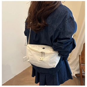 Detail of off-white pleated crescent bag with dual triangular zippers and round accent