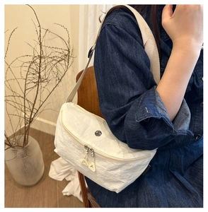 Detail of white wrinkled nylon crossbody bag with dual zippers and metal logo on a model