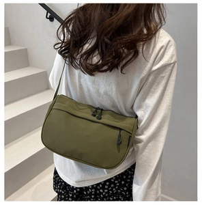 Macro detail of army green nylon crossbody bag with dual zippers and woven brand label