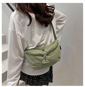 Detail of light green crossbody bag featuring dual zippers and adjustable woven strap