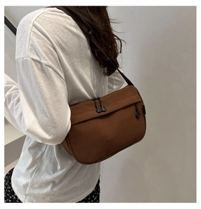 Detail of dark brown crossbody bag with multiple zippers shown worn on casual white outfit