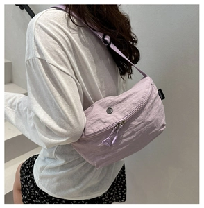 Close-up of a light purple pleated nylon crossbody bag worn by a model on stairs