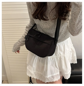 Detail of black nylon crescent crossbody bag featuring smooth zipper and side logo tag