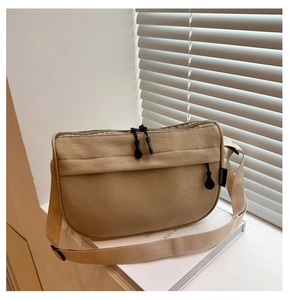 Detail of beige canvas crossbody bag with adjustable strap and dual zippers on a windowsill
