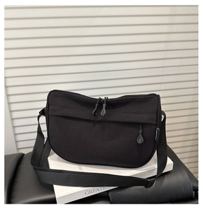 Detail of a black nylon crossbody bag with dual zippers on a minimalist book prop