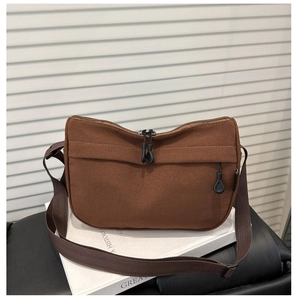 Detail of a brown canvas crossbody bag with adjustable strap and front zipper pocket
