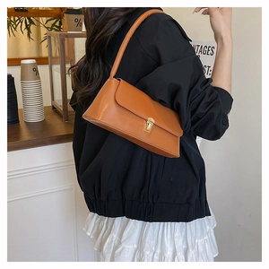 Detail view of a brown faux leather underarm bag with a golden metal buckle on a model