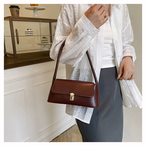 Détail d'un sac baguette en cuir marron foncé avec boucle dorée polie et finition brillante