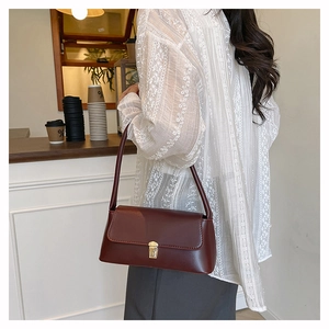 Détail du sac à bandoulière en cuir rouge foncé avec boucle dorée sur un mannequin
