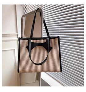Detail of beige tote bag featuring black bow ornament and pleated texture on metal stand