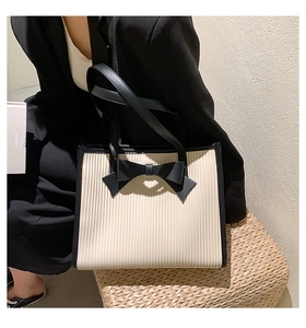 Detail of white tote bag with black bow and vertical pleated texture on straw stool