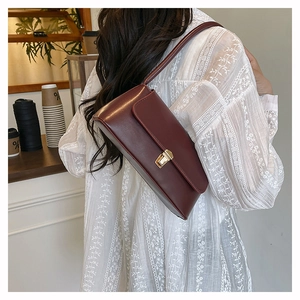 Détail du sac à bandoulière en cuir bordeaux avec fermoir doré porté par un modèle