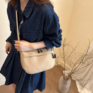 Minimalist beige canvas crescent crossbody bag shown on a model with a denim outfit