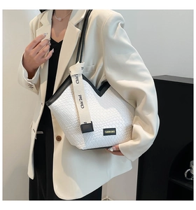Detail of white woven tote bag with black trim and branded ribbon on a white suit