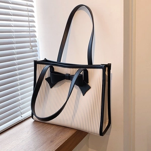 French chic off-white tote bag with black bow and leather trim on wooden windowsill