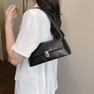 Sac sous le bras rectangulaire noir avec boucle dorée porté sur un blazer blanc chic
