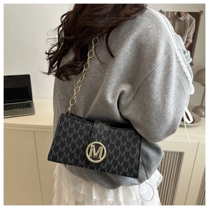 Detail of black underarm bag with M-letter print and golden circular metal logo