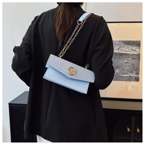 Detalle de bolso bandolera de mezclilla azul claro con hebilla M dorada en blazer negro