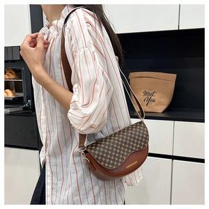 Detail of dark brown saddle bag with geometric textured flap and wide fabric shoulder strap