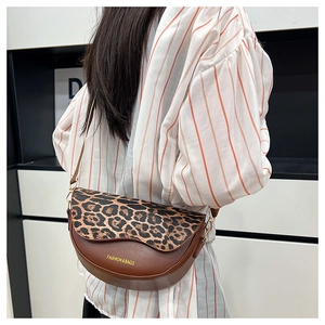 Detail of a brown leather saddle bag with leopard print flap and golden brand lettering