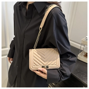 Détail du sac bandoulière beige matelassé avec chaîne dorée et fermoir pivotant en métal
