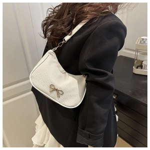 Close-up of white woven baguette bag featuring a decorative gold bow buckle and strap