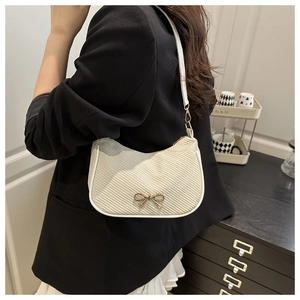 Detail of cream woven shoulder bag with gold bow hardware and elegant crescent shape