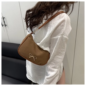 Detail of brown woven hobo bag with gold bow ornament worn on shoulder by model