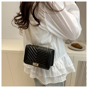 Detail of black V-quilted faux leather shoulder bag with golden chain strap and swivel lock