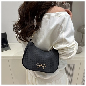 Chic black hobo bag with gold bow clasp worn as a shoulder bag in minimalist setting