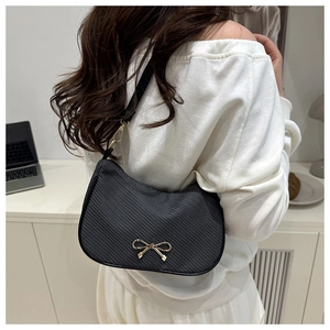 Detail of a black textured shoulder bag with an elegant golden bow metal hardware piece