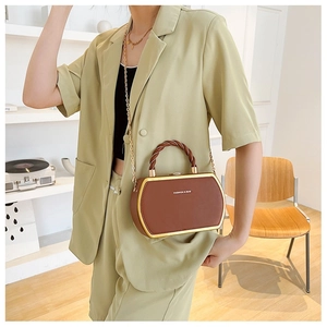 Detail of a brown hexagonal box bag with golden metal frame and woven top handle