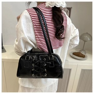 Close-up of black patent leather shoulder bag with decorative criss-cross lace detail