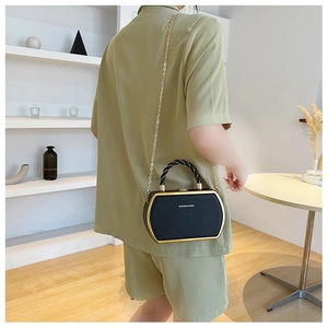 Detail of black hexagonal crossbody bag with gold frame and twisted handle on model