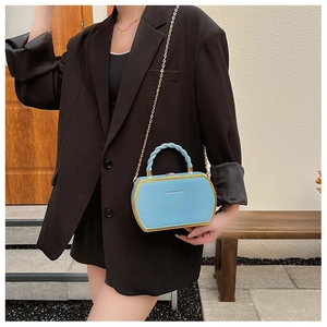 Detail of light blue box bag with golden metal frame and woven handle on black blazer