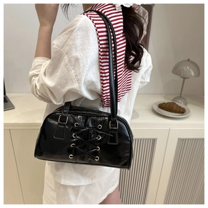 Detail of black glossy corset bag featuring lace-up design and golden metal eyelets