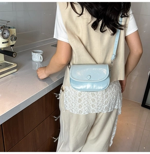 Detail of light blue crossbody bag with glossy finish and silver hardware on marble surface