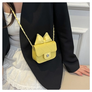 Detail of yellow quilted crossbody bag featuring a large bow and camellia metal clasp