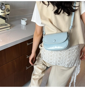 Close-up of a light blue glossy patent leather saddle bag with round buckle detail