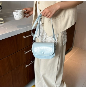 Close-up of light blue saddle bag with glossy finish and adjustable shoulder strap