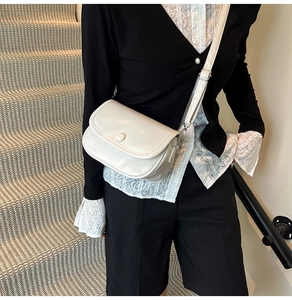 Close-up of cream retro saddle bag with adjustable strap worn by a female model
