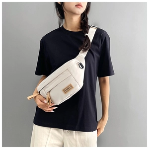 Detail of minimalist cream crossbody bag with adjustable strap and leather logo patch