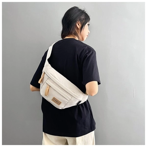 Detail of adjustable nylon strap and beige canvas saddle bag worn by a model