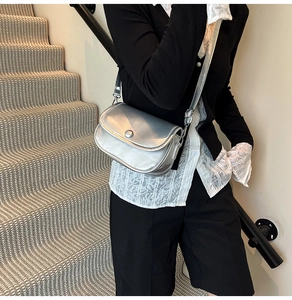 Detail of silver metallic crossbody bag with round buckle and sleek shoulder strap